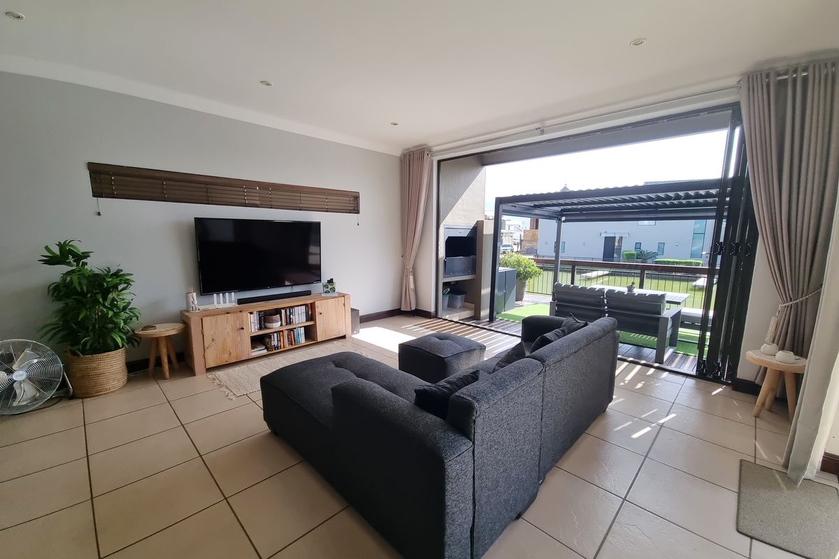 Spacious living room featuring tiled flooring, recessed lighting, and large stacking doors that open onto a covered patio with a built-in braai.