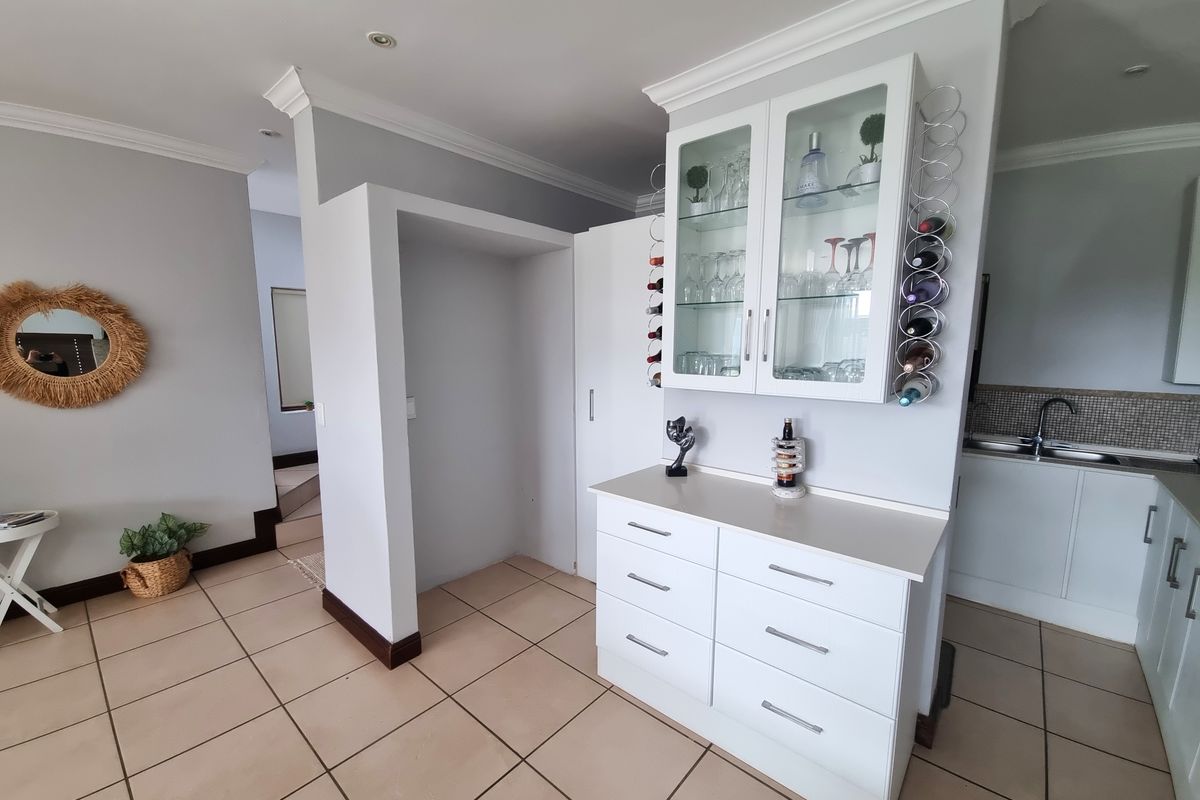 A well-maintained kitchen area featuring white cabinetry, a built-in wine rack, glass-fronted display units, and neutral tiled flooring.