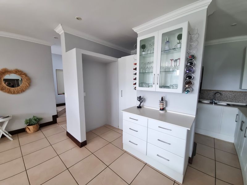 A well-maintained kitchen area featuring white cabinetry, a built-in wine rack, glass-fronted display units, and neutral tiled flooring.