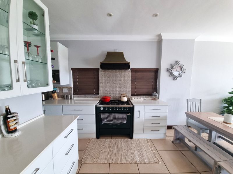 A well-maintained kitchen featuring white cabinetry, stone countertops, a gas stove with a feature extractor fan, and a tiled backsplash.