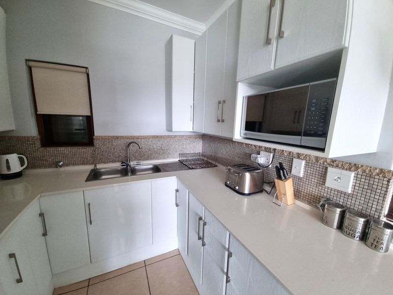 A clean and functional kitchen featuring white cabinetry, stone countertops, a mosaic tile backsplash, and a built-in microwave.
