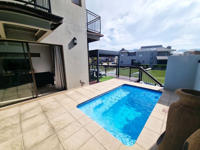 Outdoor pool area featuring a tiled deck, adjacent wooden patio with pergola, and direct access to the home via sliding glass doors.