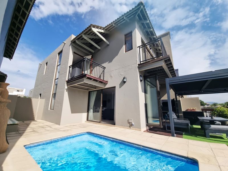 Rear exterior view featuring a swimming pool, tiled patio area, pergola, and upper-level balconies with modern architectural design.