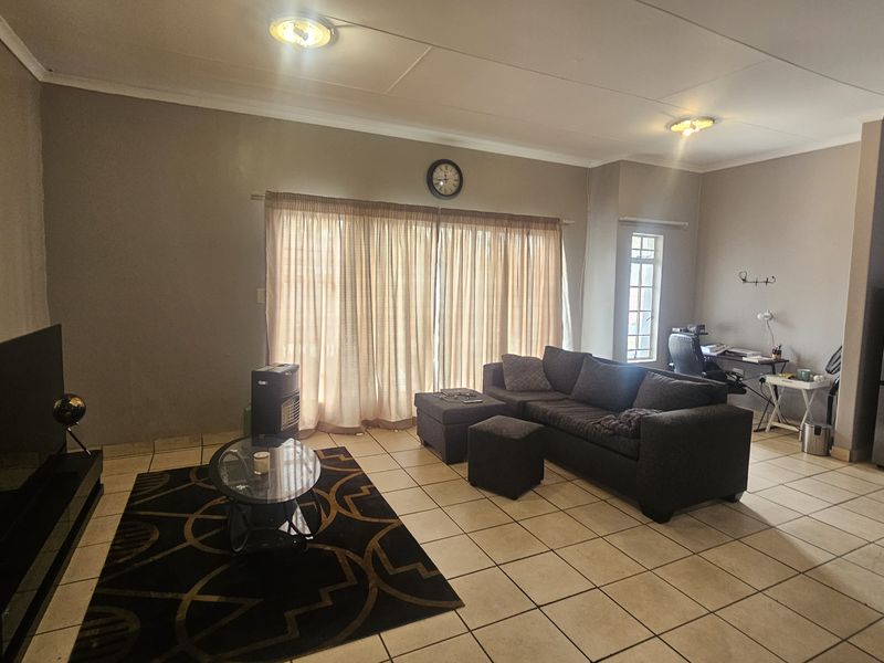 An open-plan living area featuring ceramic floor tiles, large sliding glass doors with curtains, and recessed ceiling lighting.