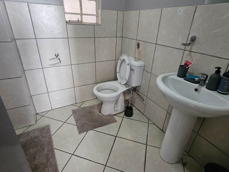 A functional bathroom featuring a pedestal basin, a standard toilet, and full-height wall tiling.