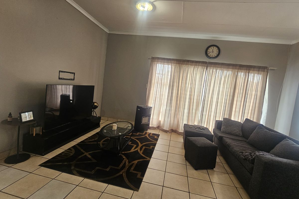 A spacious living room featuring neutral wall tones, tiled flooring, and large windows with curtains, providing a comfortable and functional living space.