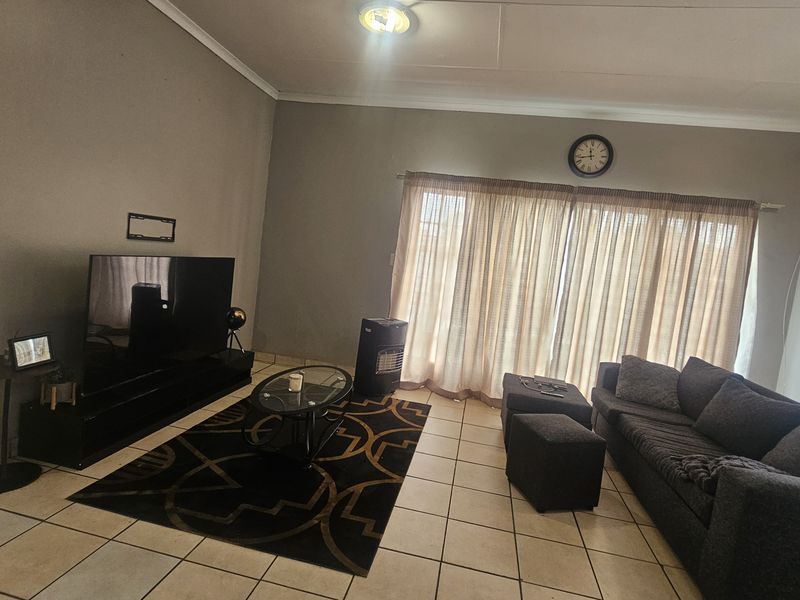 A spacious living room featuring neutral wall tones, tiled flooring, and large windows with curtains, providing a comfortable and functional living space.
