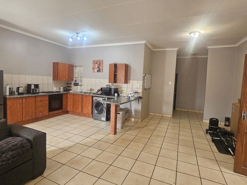 Open-plan kitchen and living area featuring tiled flooring, wooden cabinetry, built-in oven, and integrated laundry space.