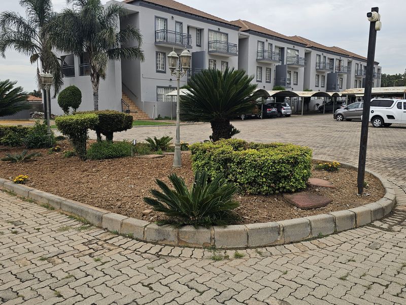 Exterior view of an apartment complex featuring paved parking areas, landscaped garden beds with mature shrubs, and covered parking bays.