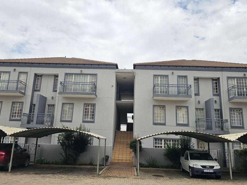 Exterior view of a multi-story apartment complex featuring balconies, tiled roof, and covered parking bays.