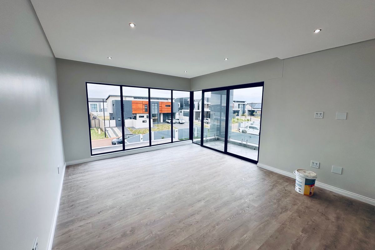A bright, modern, and empty living room featuring large floor-to-ceiling windows, sliding glass doors, and contemporary laminate flooring.