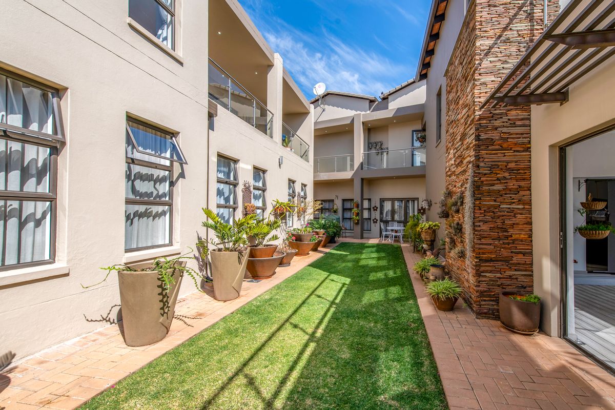 A well-maintained rear courtyard featuring a central lawn, paved pathways, stone cladding feature wall, and upper-level balconies with glass balustrades.