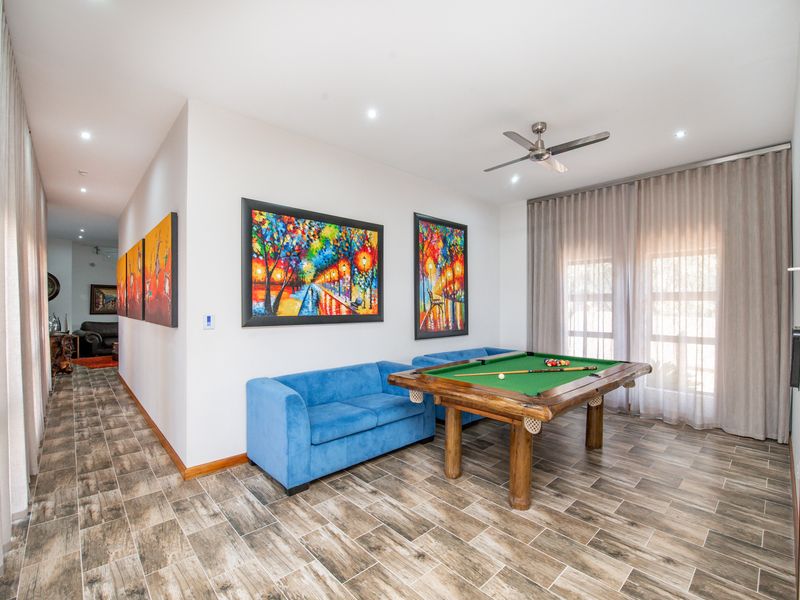 Spacious living area featuring wood-look tiled flooring, recessed lighting, and a ceiling fan, with large windows dressed in floor-to-ceiling curtains.