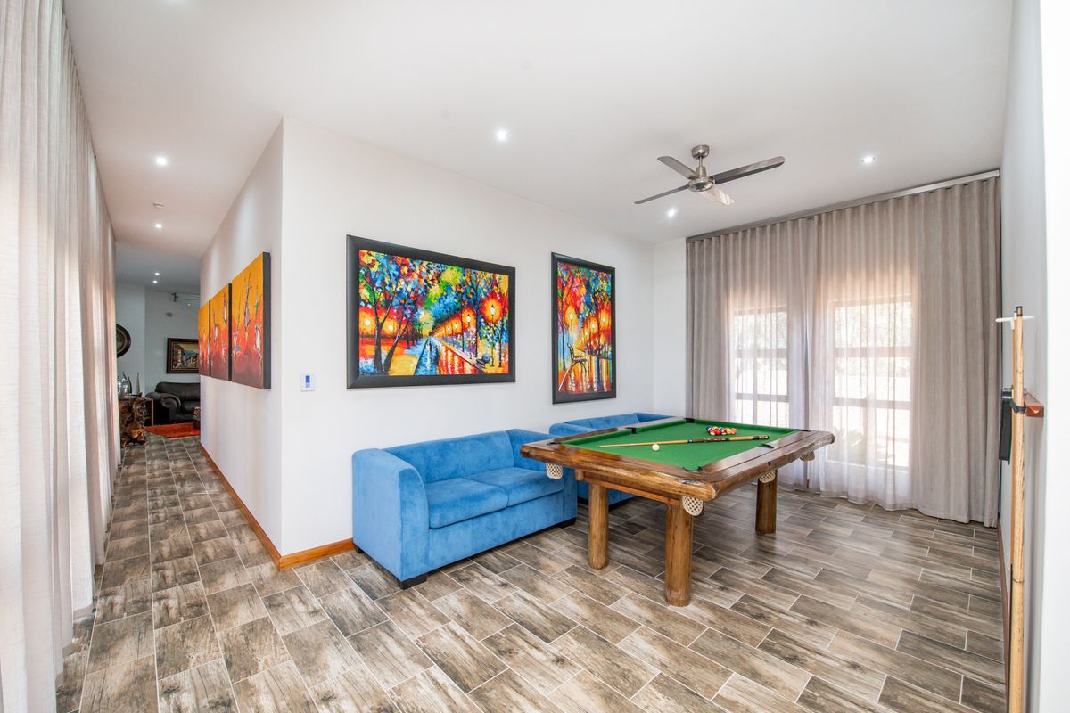 Spacious living area featuring wood-look tiled flooring, recessed lighting, and a ceiling fan, with large windows dressed in floor-to-ceiling curtains.