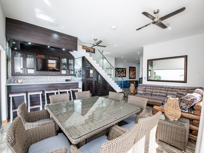 Spacious open-plan living area featuring a built-in bar, integrated wine storage, glass staircase railing, and modern ceiling fans, creating a versatile entertainment space.