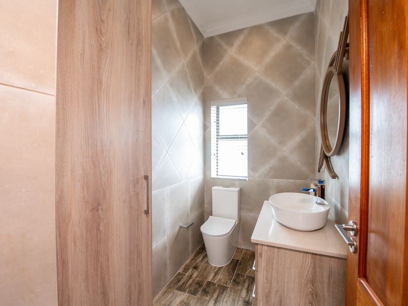 A modern guest bathroom featuring a vessel sink on a wood-finish vanity, diamond-pattern wall tiles, and wood-look floor tiles.