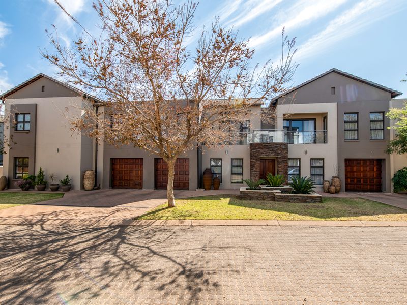 Modern double-story residential facade featuring a triple garage, stone-clad entrance detail, and a glass-fronted balcony, set within a well-maintained landscaped environment.