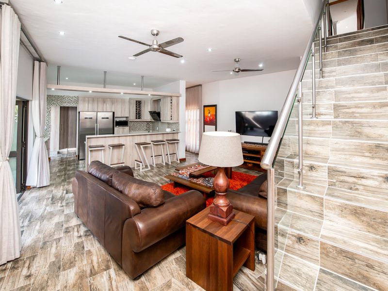 Open-plan living area featuring a modern kitchen with island, tiled flooring throughout, and a staircase with a stainless steel and glass balustrade.
