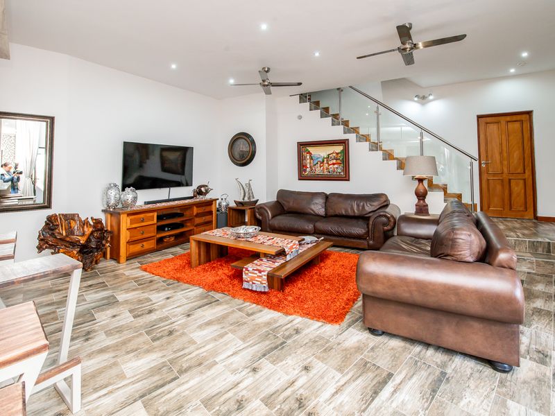 Spacious open-plan living area featuring modern tiled flooring, recessed lighting, ceiling fans, and a contemporary staircase with a glass balustrade.