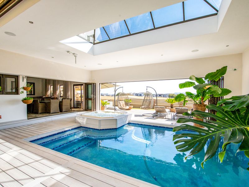 Luxurious indoor pool area featuring a built-in spa, large skylight, and seamless transition to the outdoor patio through expansive bi-fold doors.