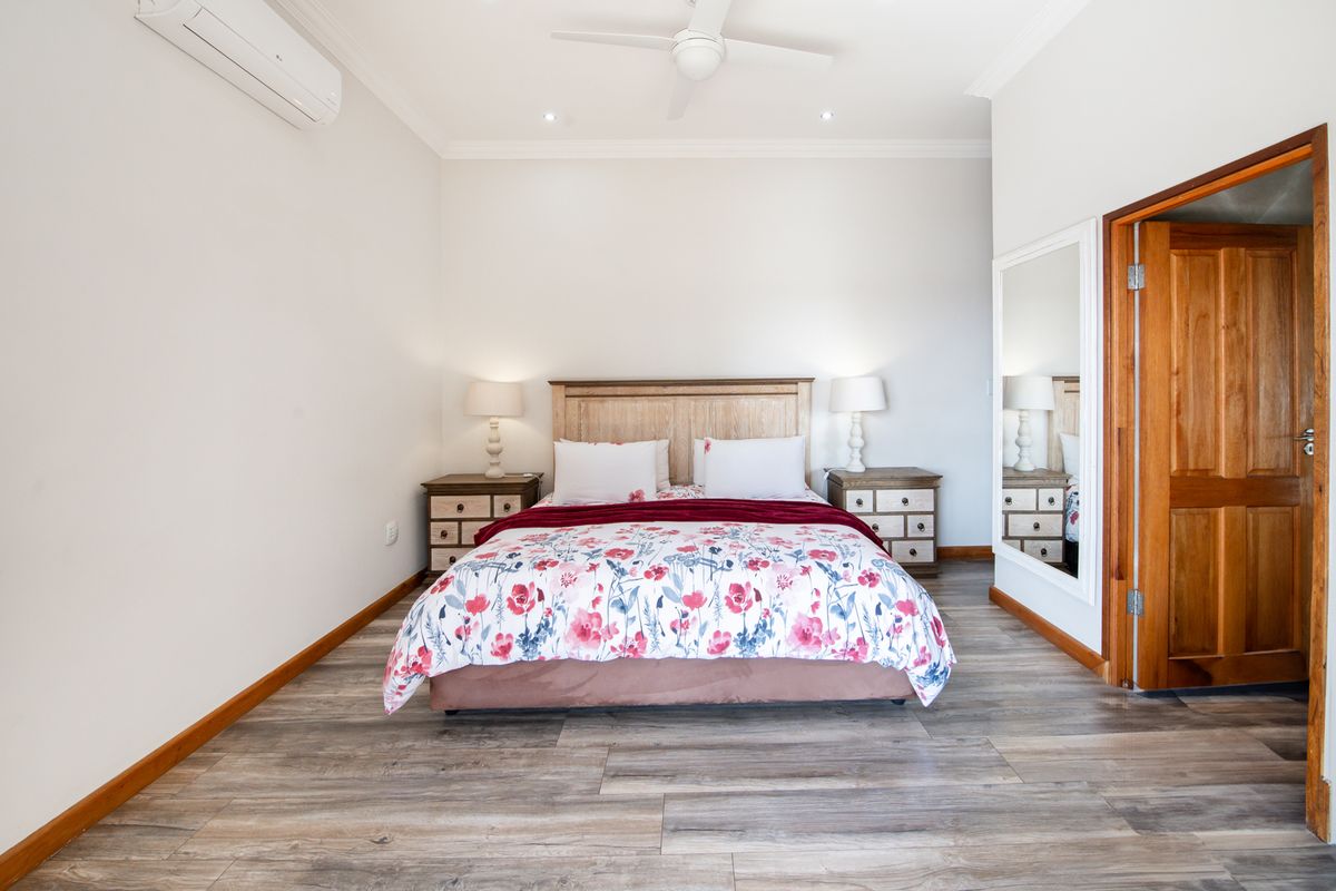 A well-maintained bedroom featuring laminate flooring, a ceiling fan, and a wall-mounted split-system air conditioner.