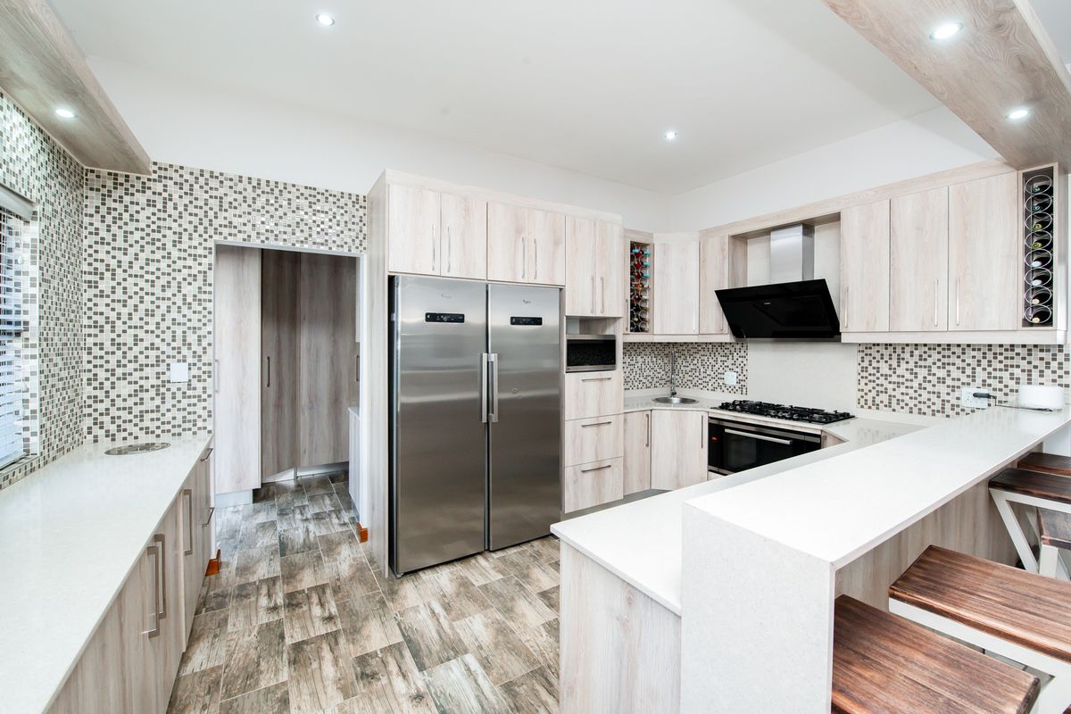 Modern kitchen featuring light wood cabinetry, stone countertops, mosaic tile backsplash, integrated appliances, and a breakfast bar with recessed lighting.