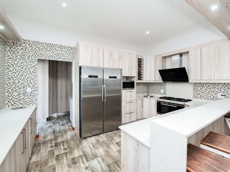 Modern kitchen featuring light wood cabinetry, stone countertops, mosaic tile backsplash, integrated appliances, and a breakfast bar with recessed lighting.
