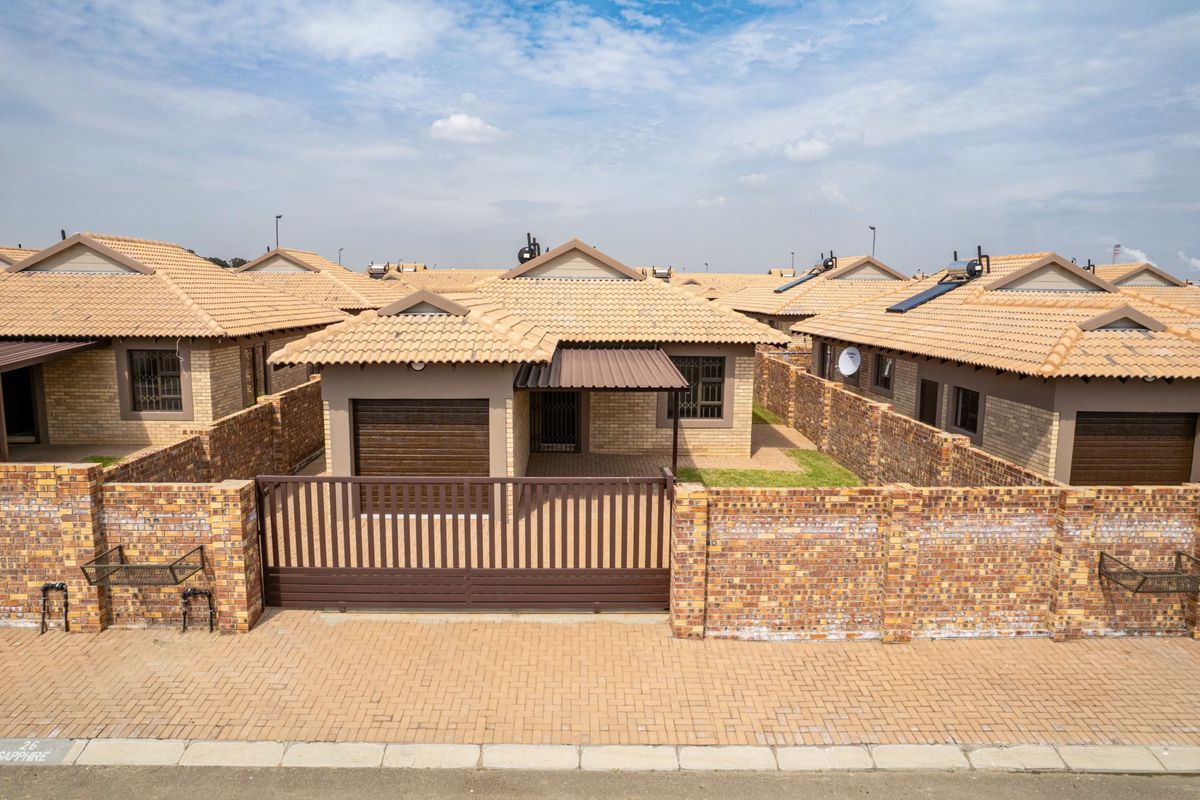 Aerial view of a residential property featuring a brick facade, tiled roof, solar water heater, and a secure gated entrance with a paved driveway.