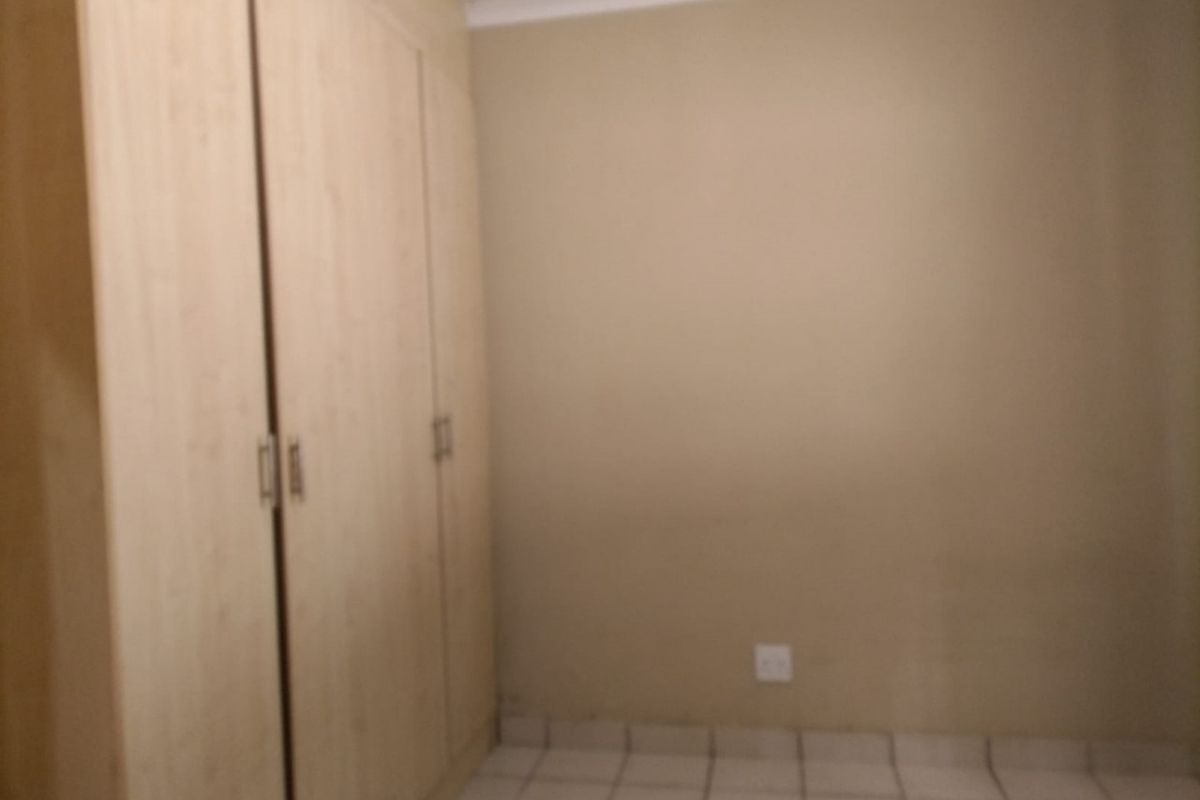 A simple bedroom featuring light wood-finish built-in cupboards and neutral tiled flooring, providing a clean and functional space.
