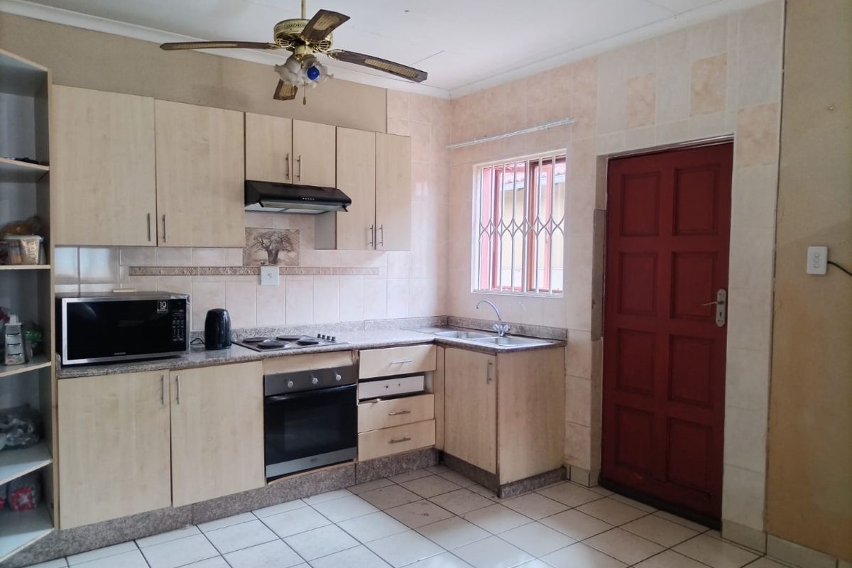 Functional kitchen featuring light wood cabinetry, built-in oven and hob, tiled splashbacks, and tiled flooring with direct access to an exterior door.