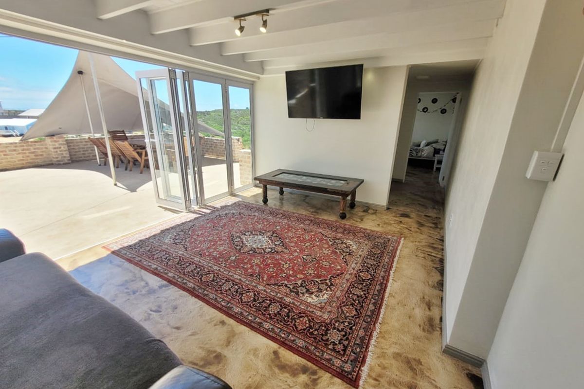 Living room featuring polished concrete floors, exposed beam ceiling, and large bi-fold doors opening onto an outdoor patio area.