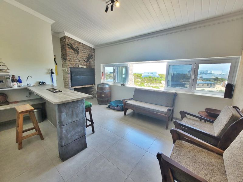 Open plan living area featuring a built-in bar, brick fireplace, tiled flooring, and large windows with coastal views.