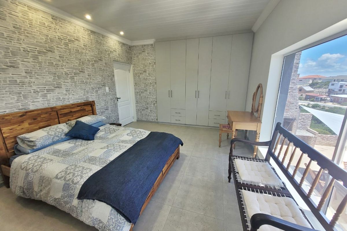 Spacious bedroom featuring a stone-cladding accent wall, extensive built-in cupboards, tiled flooring, and large windows offering natural light and exterior views.