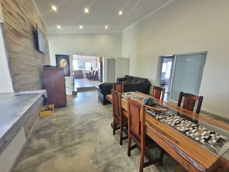 Spacious open-plan living and dining area featuring polished concrete floors, a textured stone feature wall, and recessed lighting.