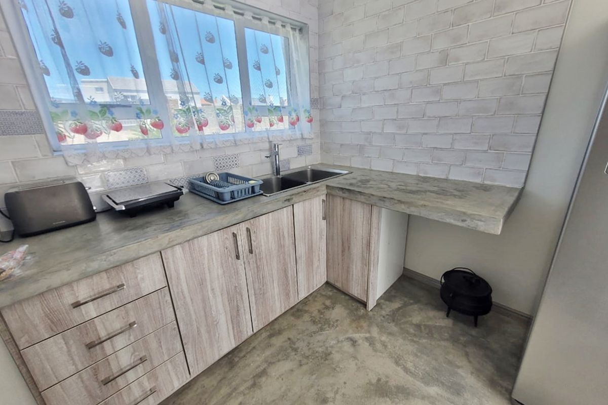 A functional kitchen featuring laminate cabinetry, concrete-look countertops, a stainless steel double sink, and a stylish subway tile backsplash.