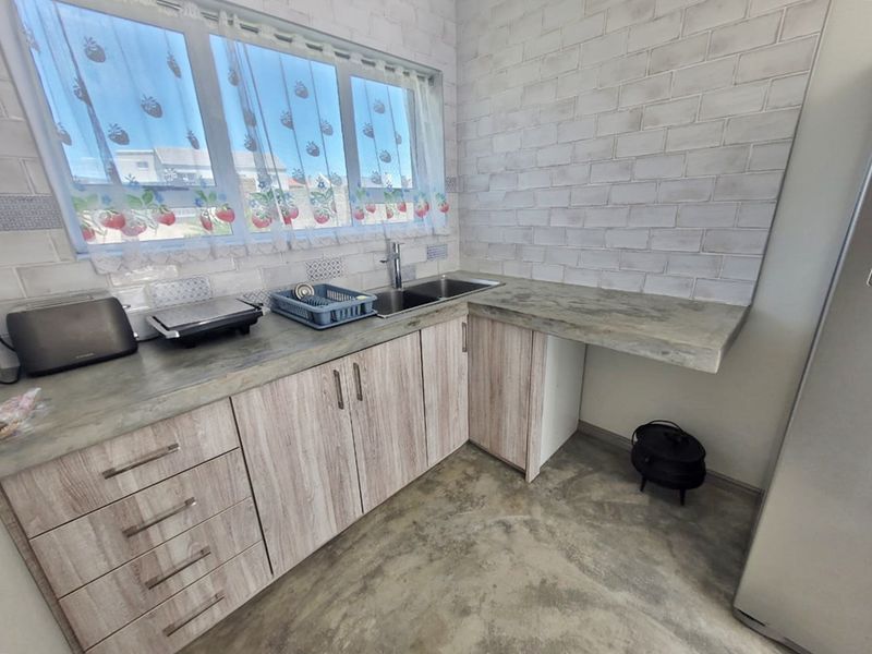 A functional kitchen featuring laminate cabinetry, concrete-look countertops, a stainless steel double sink, and a stylish subway tile backsplash.