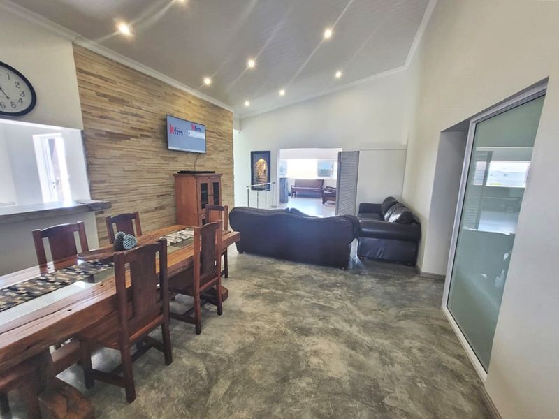 Spacious open-plan living and dining area featuring polished concrete floors, a timber feature wall, and vaulted ceilings with recessed lighting.