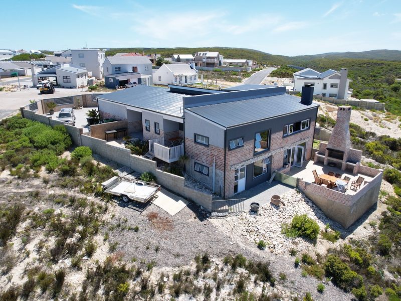 Aerial view of a modern two-story house featuring a metal roof, brick chimney, and an outdoor patio area with a built-in fireplace.