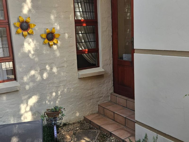 A small outdoor patio area featuring tiled steps leading to a timber door, with textured exterior walls and timber-framed windows.
