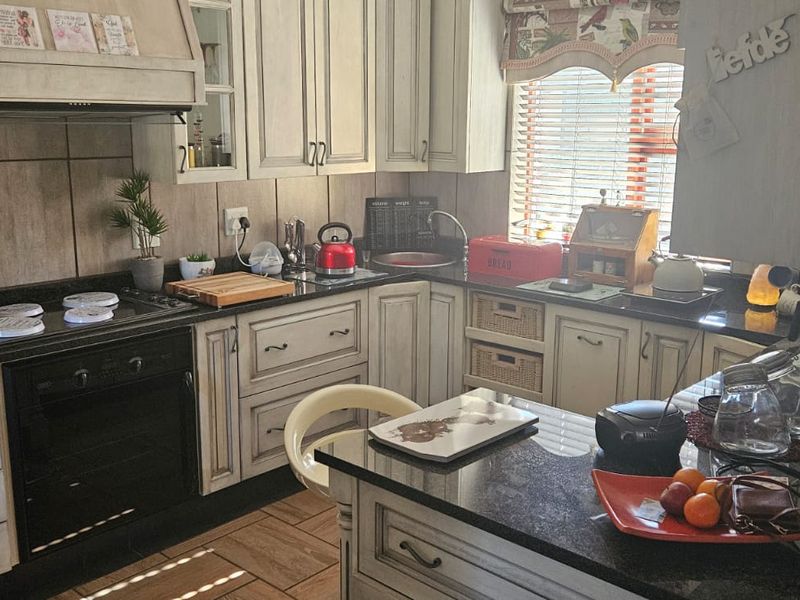 A functional kitchen featuring granite countertops, built-in oven, hob, extractor fan, and custom cabinetry with a tiled backsplash and ceramic floor tiles.