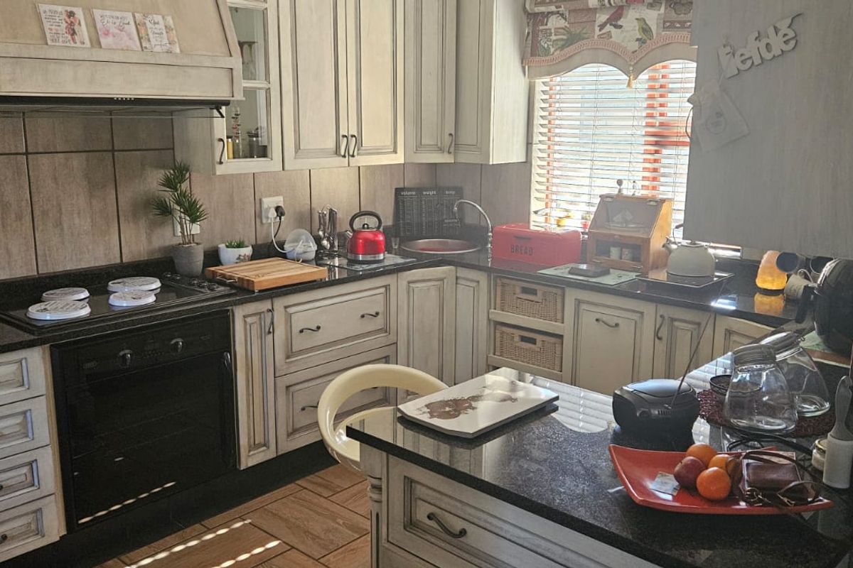 A functional kitchen featuring granite countertops, built-in oven, hob, extractor fan, and custom cabinetry with a tiled backsplash and ceramic floor tiles.