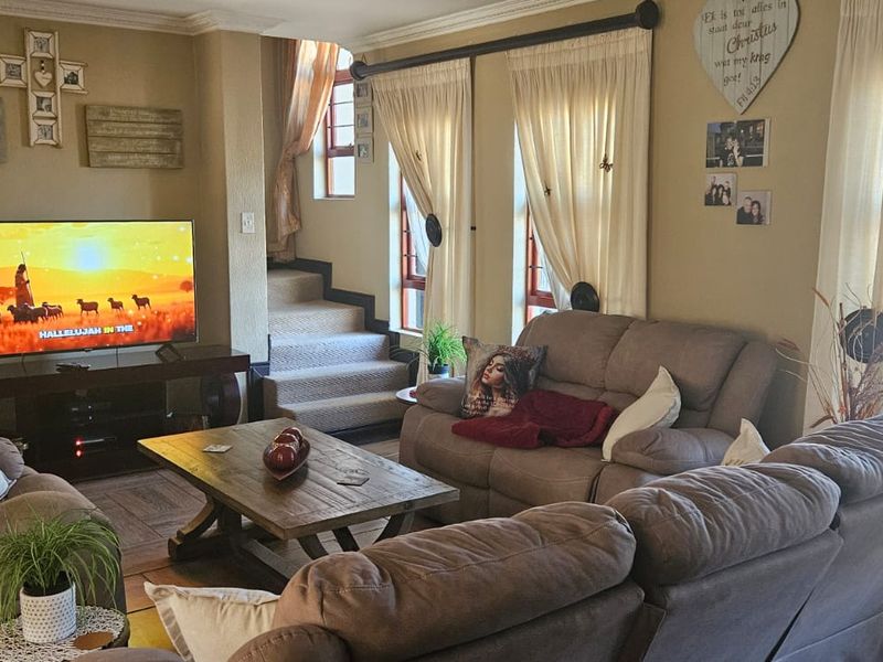 A comfortable living room featuring tiled flooring, a staircase leading to the upper level, and large windows allowing for natural light.