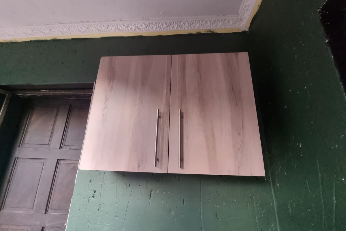 A close-up view of wall-mounted kitchen cabinetry featuring wood-grain finish doors and modern metal handles against a dark green painted wall.
