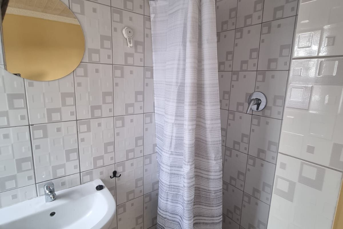 A functional bathroom featuring a pedestal sink, a shower with a rainfall showerhead, and patterned wall tiling.