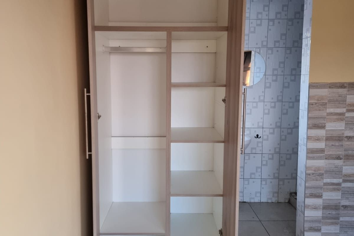 A bedroom featuring a built-in wooden wardrobe with shelving and hanging space, finished with tiled flooring and ceiling cornice detail.