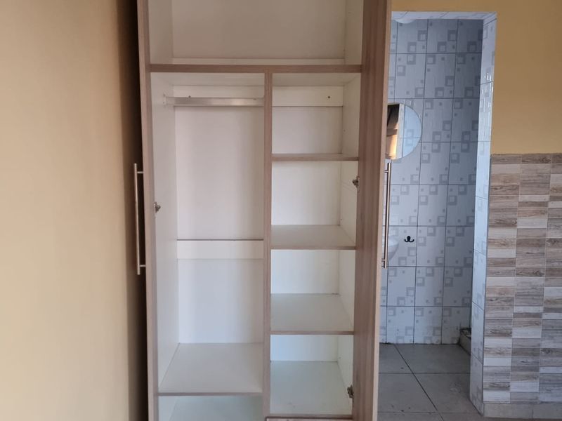 A bedroom featuring a built-in wooden wardrobe with shelving and hanging space, finished with tiled flooring and ceiling cornice detail.