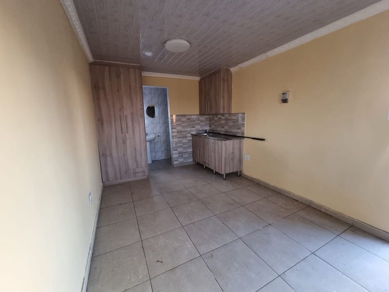 An open-plan living area featuring tiled floors, built-in cupboards, and a compact kitchenette with sink, offering a functional blank canvas for potential updates.