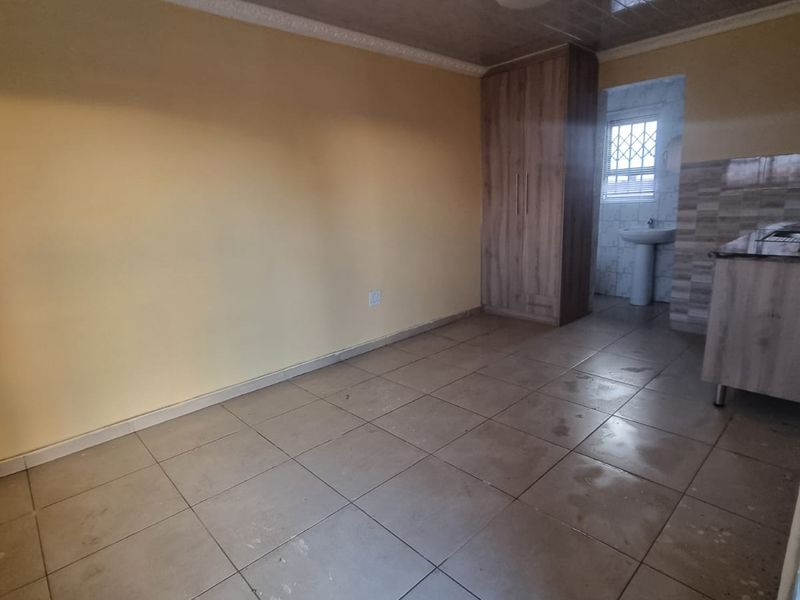 Open plan living area featuring tiled flooring, a built-in cupboard, and an adjoining space with a pedestal basin and security window.