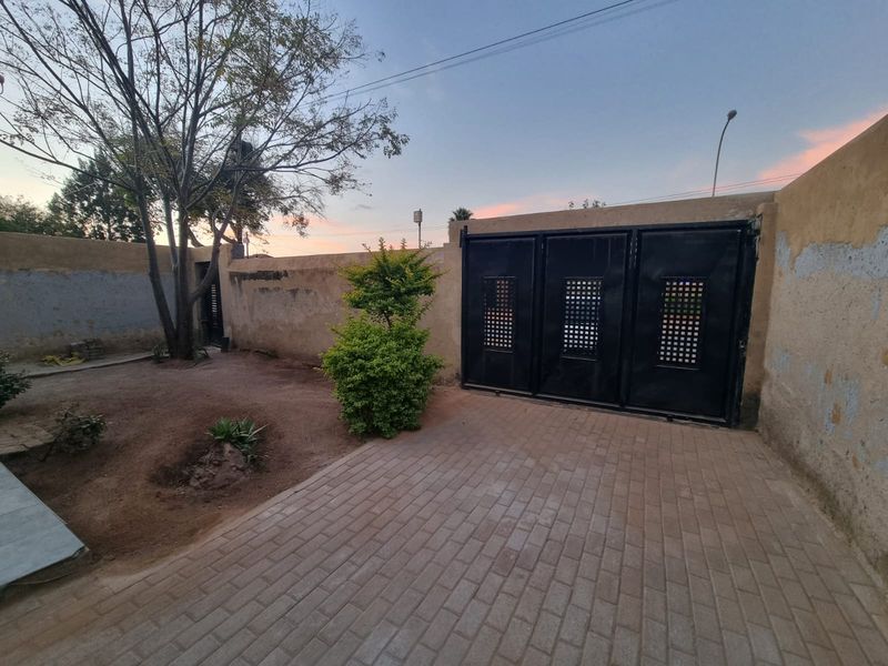 Rear exterior area featuring a paved driveway, secure metal gate, and perimeter walling with some visible wear to the wall finishes.