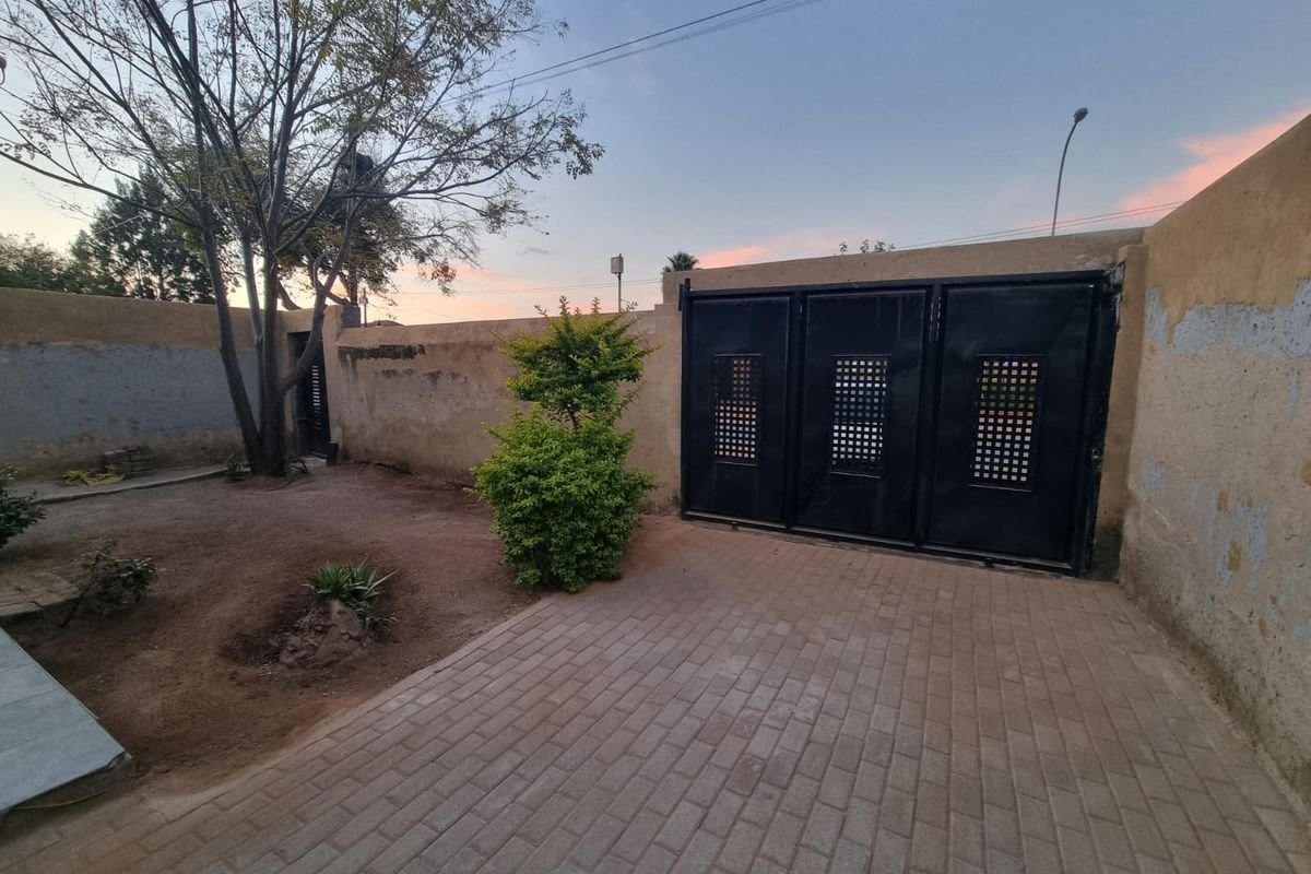 Rear exterior area featuring a paved driveway, secure metal gate, and perimeter walling with some visible wear to the wall finishes.